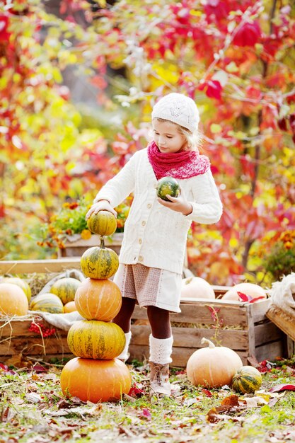 Niña linda que juega con las calabazas en parque del otoño. Actividades de otoño para niños. Adorable niña construye una torre de calabazas.