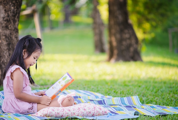 Una niña linda que lee un libro sentado debajo del árbol