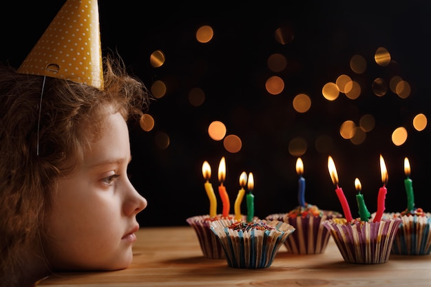 Niña linda que mira las velas en las tortas de cumpleaños.