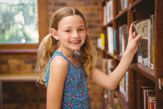 Niña linda que selecciona el libro en biblioteca