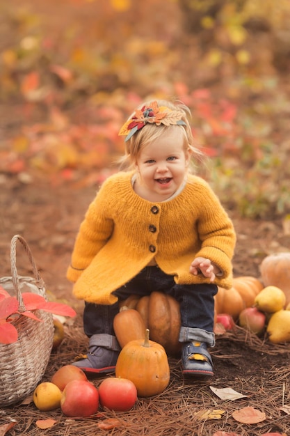 Niña linda que se sienta en la calabaza y que juega en bosque del otoño