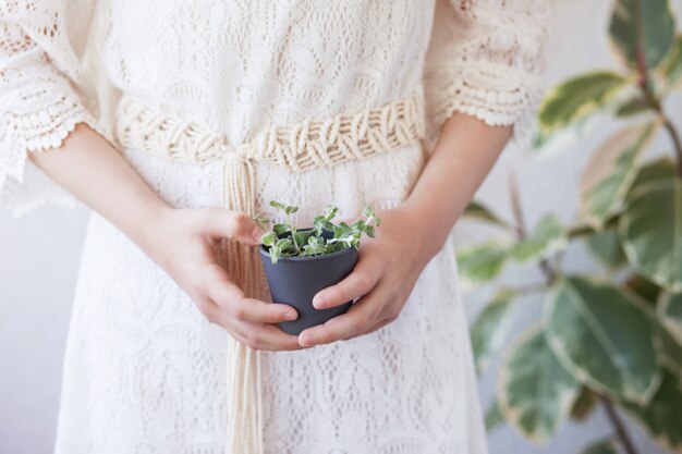 Niña linda que sostiene una maceta del jardín con una planta verde joven.