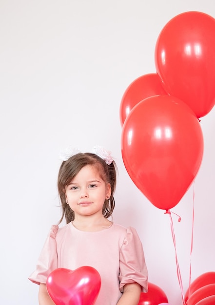 Niña linda que sostiene un manojo de globos rojos en forma de corazón