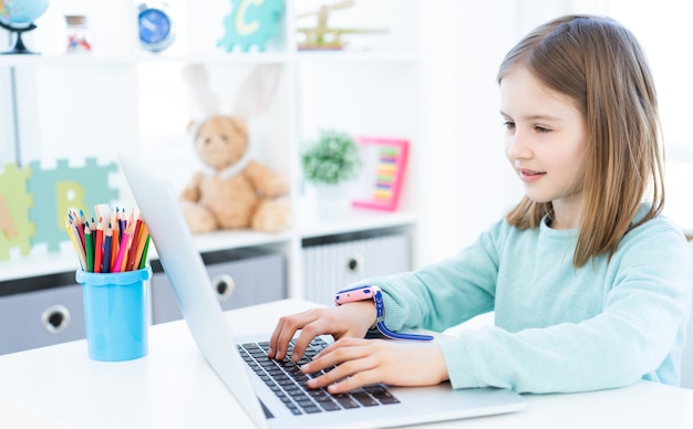 Niña linda que usa la computadora en la habitación de la luz