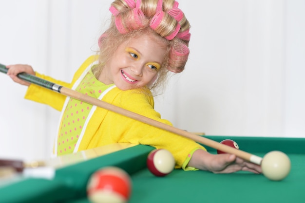 Niña linda en rizadores de pelo jugando al billar