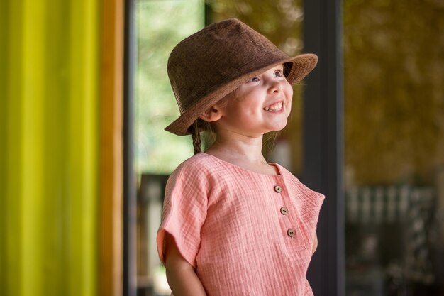 Niña linda en ropa de muselina y sombrero marrón de estilo rural sobre fondo de madera en un día de verano