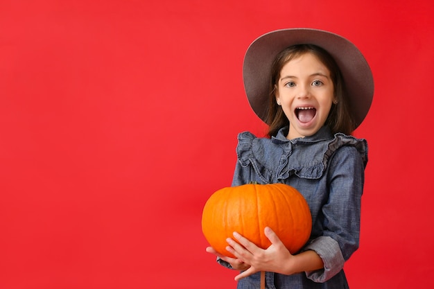 Niña linda en ropa de otoño y con calabaza en rojo