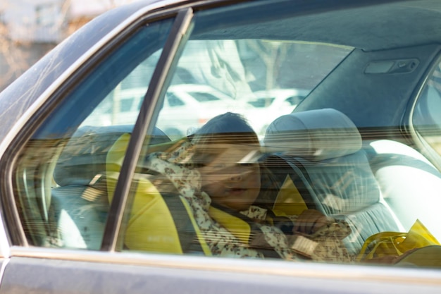 Niña linda sentada en un asiento de coche para niños en el coche mirando por la ventana