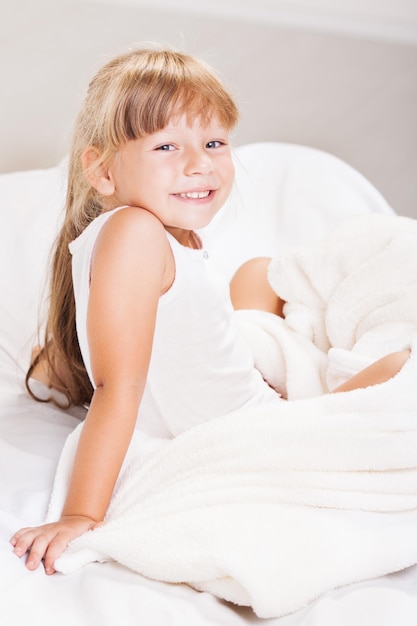 Niña linda sentada en la cama por la mañana.