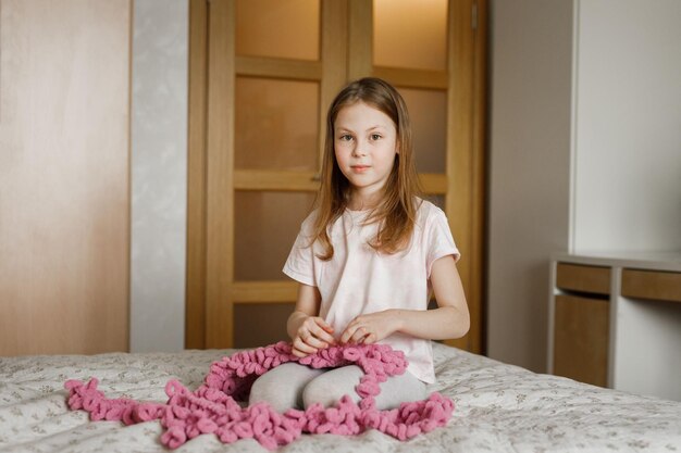 Niña linda sentada con costura en la cama en el dormitorio