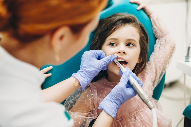 Niña linda sentada en una silla de estomatología tras una cirugía de dientes por un dentista pediátrico.