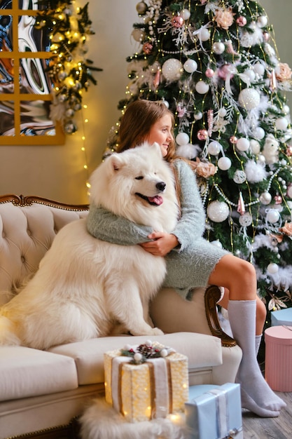 Niña linda sentada en el sofá con perro samoyedo