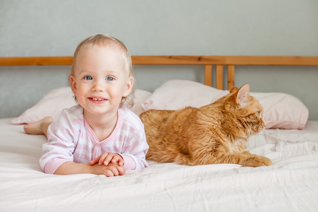 Foto una niña linda se sienta en la cama con un gato gordo de jengibre acaricia y juega con él