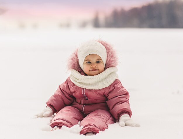 Una niña linda se sienta en la nieve en el invierno al aire libre