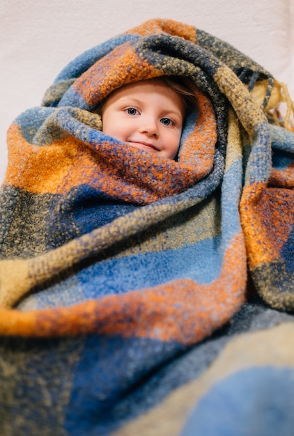 Foto niña linda se sienta en su habitación envuelta en una colcha