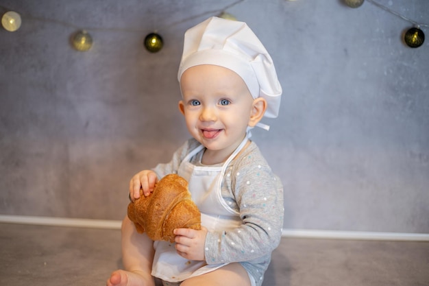 Una niña linda con un sombrero de chef y un delantal se sienta en casa en la mesa de la cocina