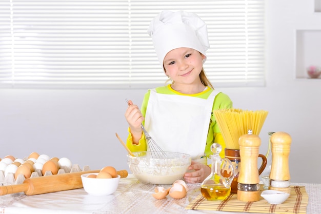 Niña linda con sombrero de chef horneando pastel en la cocina