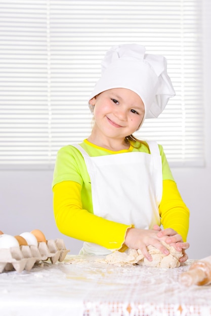 Niña linda con sombrero de chef horneando pastel en la cocina