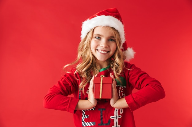 Niña linda con sombrero de Navidad que se encuentran aisladas, sosteniendo el cuadro actual