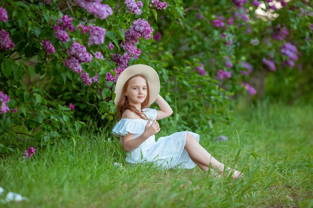 Niña linda en un sombrero de paja en primavera en el jardín lila