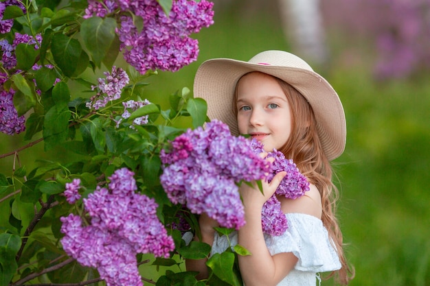 Niña linda en un sombrero de paja en primavera en el jardín lila