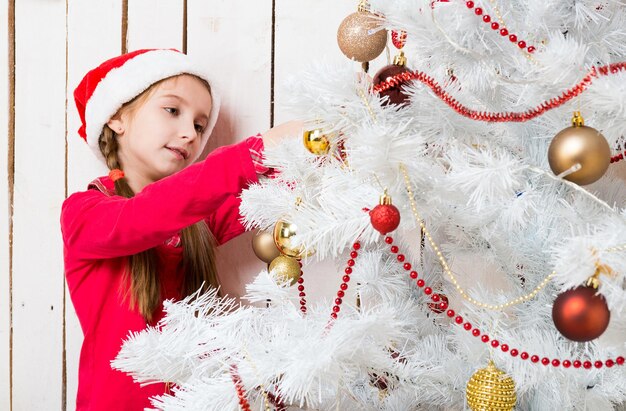 Foto una niña linda con sombrero rojo de santa decorando el árbol de año nuevo