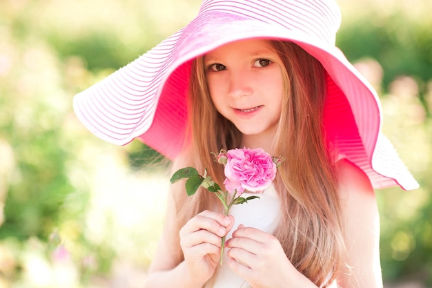 Niña linda con sombrero rosa grande sosteniendo flores al aire libre