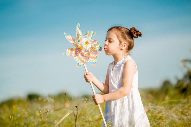 Niña linda sonriendo verano en el campo con un molino de viento