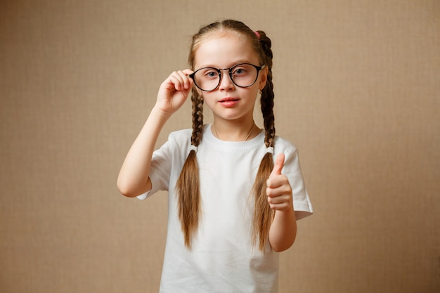 Niña linda sonriente con anteojos negros que muestran los pulgares para arriba