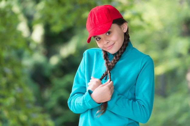 Una niña con una linda sonrisa sostiene largas trenzas morenas con un estilo casual de moda y un paisaje natural