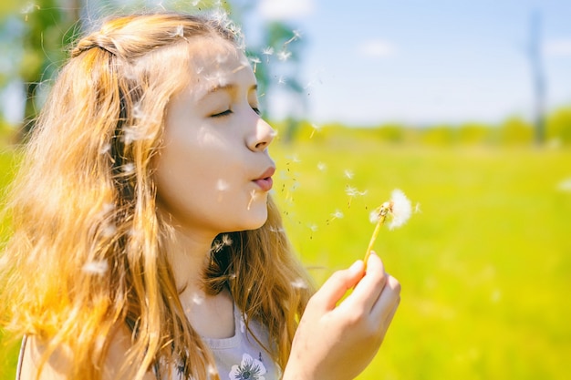 Niña linda sopla dientes de león en un día soleado al aire libre