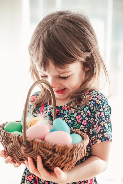 Niña linda sosteniendo una canasta llena de huevos de Pascua de colores pastel