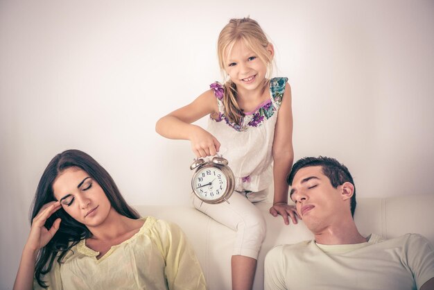 Niña linda sosteniendo un despertador y despertando a sus padres