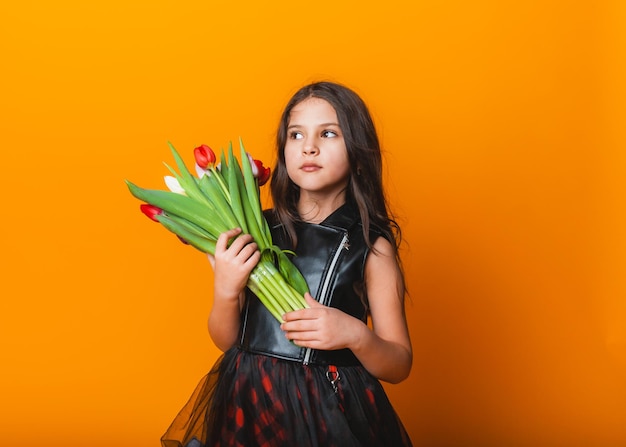 Niña linda sosteniendo un ramo de tulipanes sobre un fondo amarillo Feliz día de la mujer Lugar para texto Emociones vívidas 8 de marzo