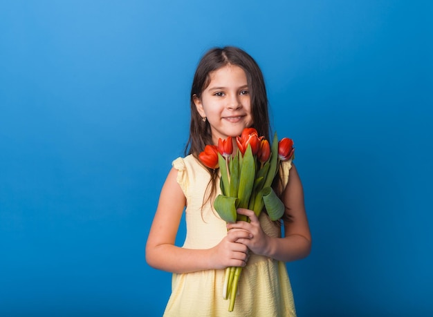 Niña linda sosteniendo un ramo de tulipanes sobre un fondo azul Feliz día de la mujer Lugar para texto Emociones vívidas 8 de marzo