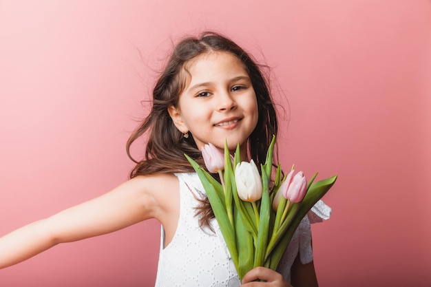 Niña linda sosteniendo un ramo de tulipanes sobre un fondo rosa Feliz día de la mujer Lugar para texto Emociones vívidas 8 de marzo