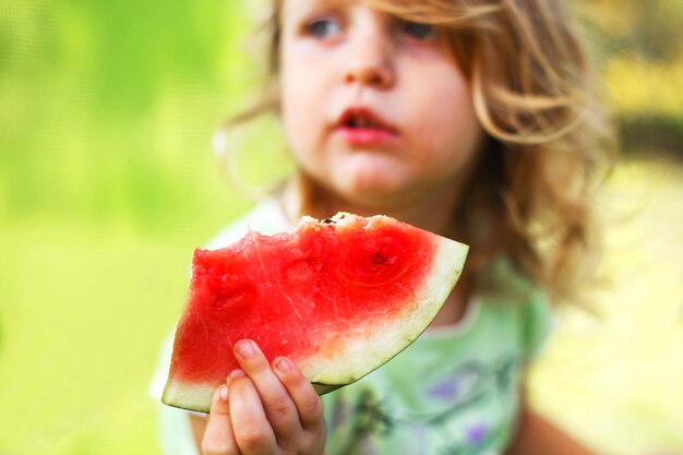 Niña linda sosteniendo un trozo de sandía cerca en el jardín en verano