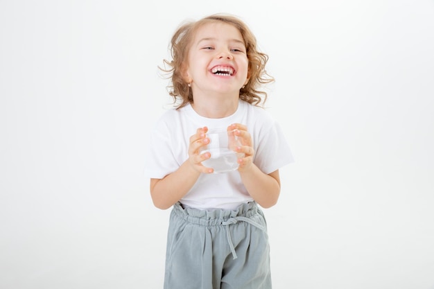 Una niña linda sostiene una jarra de agua y vierte agua en un vaso aislado en un fondo blanco