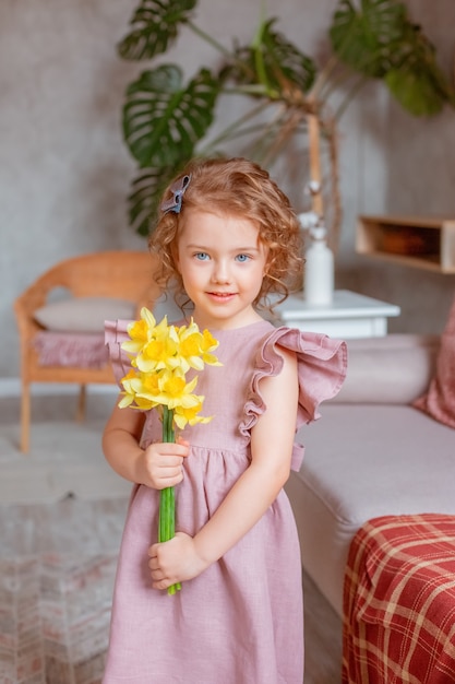 Niña linda sostiene un ramo de narcisos en casa