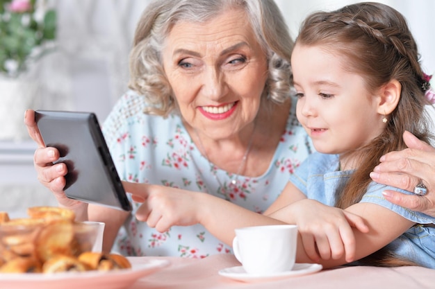 Niña linda con su abuela mirando la tableta