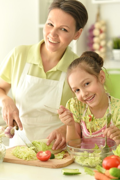 Niña linda con su madre cocinando juntos en la mesa de la cocina