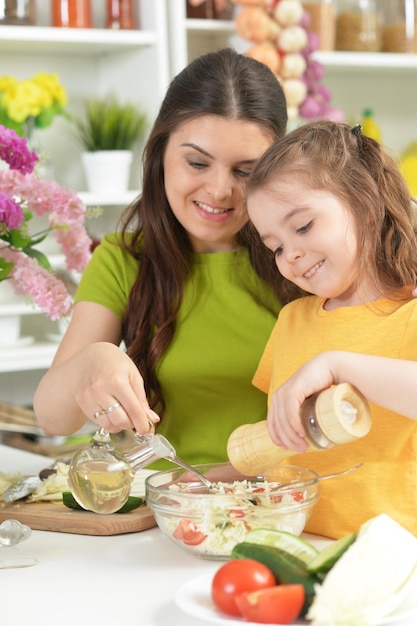 Niña linda con su madre cocinando juntos en la mesa de la cocina