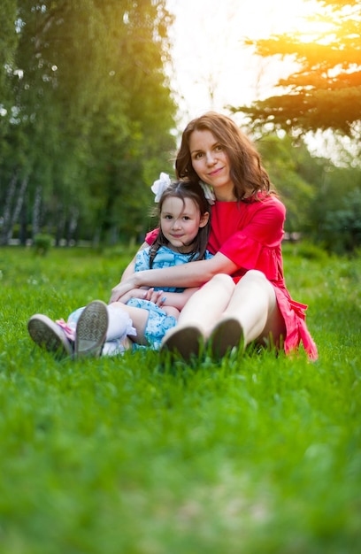 Niña linda y su madre divirtiéndose en el césped en un parque soleado