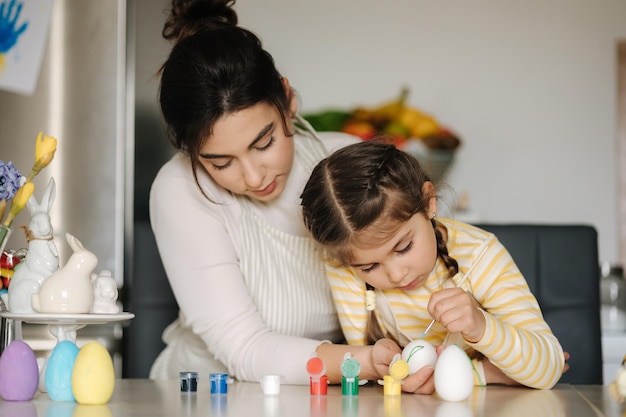 Una niña linda con su madre preparándose para pintar huevos de Pascua madre e hija se miran