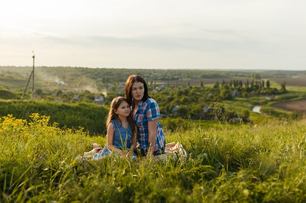 Niña linda con su madre sentada al atardecer