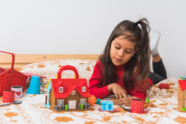 Foto niña linda en suéter rojo de camiseta de cuello largo jugando con sus juguetes en el dormitorio.