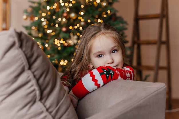 Niña linda en suéter rojo de navidad juega junto al árbol de navidad en casa. decoración de año nuevo.