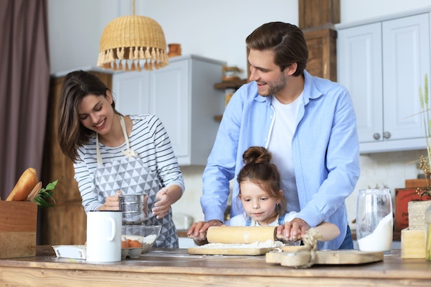 Niña linda y sus padres se divierten mientras cocinan juntos en la cocina en casa.