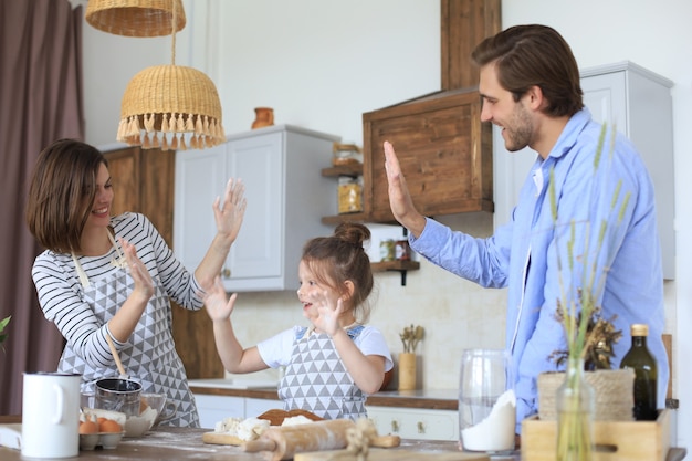 Niña linda y sus padres se divierten mientras cocinan juntos en la cocina en casa.