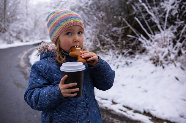 Foto una niña linda con una taza de té y un hombre de jengibre en un día nevado de invierno